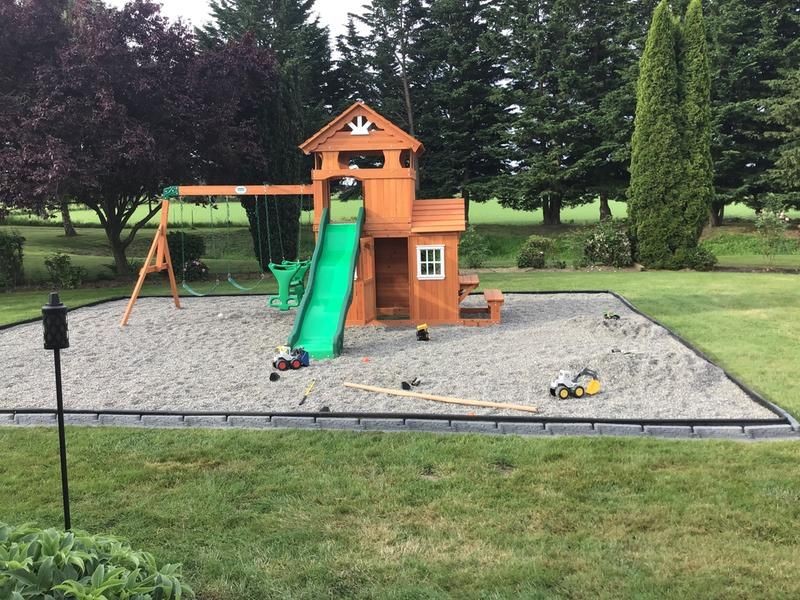 Playground with wooden playset, slide, and swings in a grassy backyard surrounded by trees.