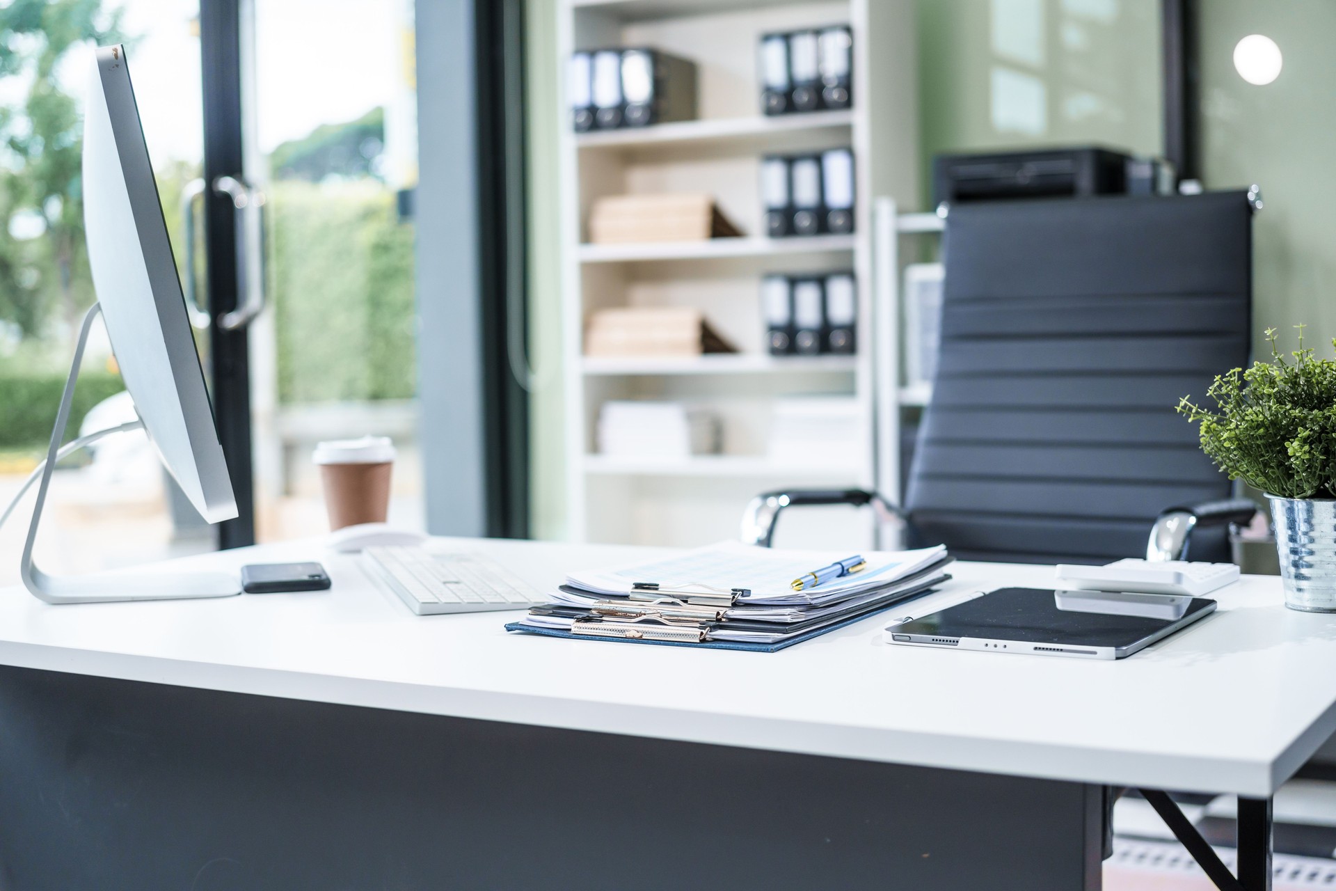 A desk in the office is neatly organized with a computer monitor, document, tablet, and telephone placed on it. The setup is ready for efficient work and smooth communication.